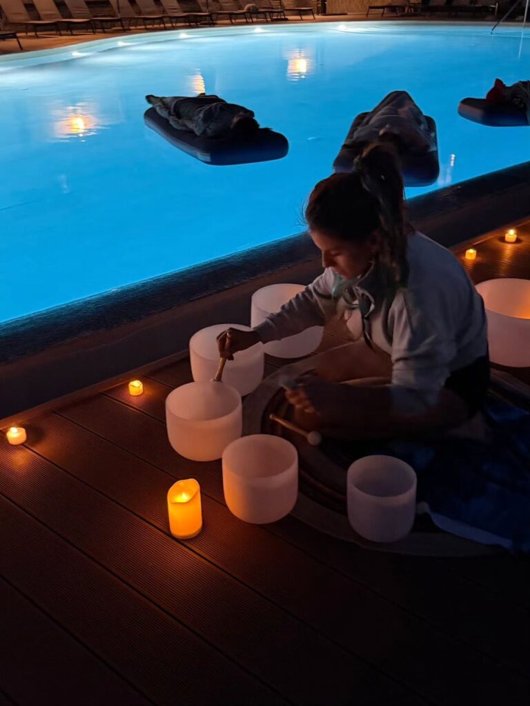 Woman playing crystal bowls by a candlelit pool at night, creating a serene and peaceful atmosphere.