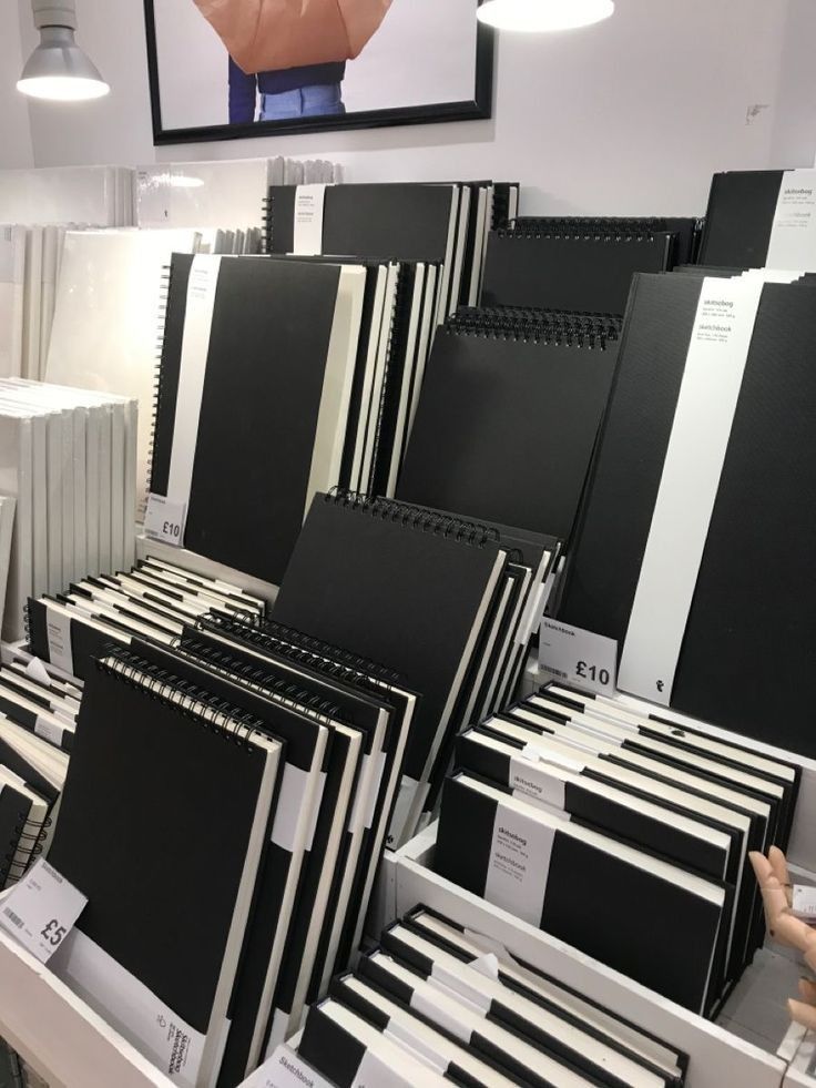 Display of various black sketchbooks on shelves in a store lit by overhead lamps.