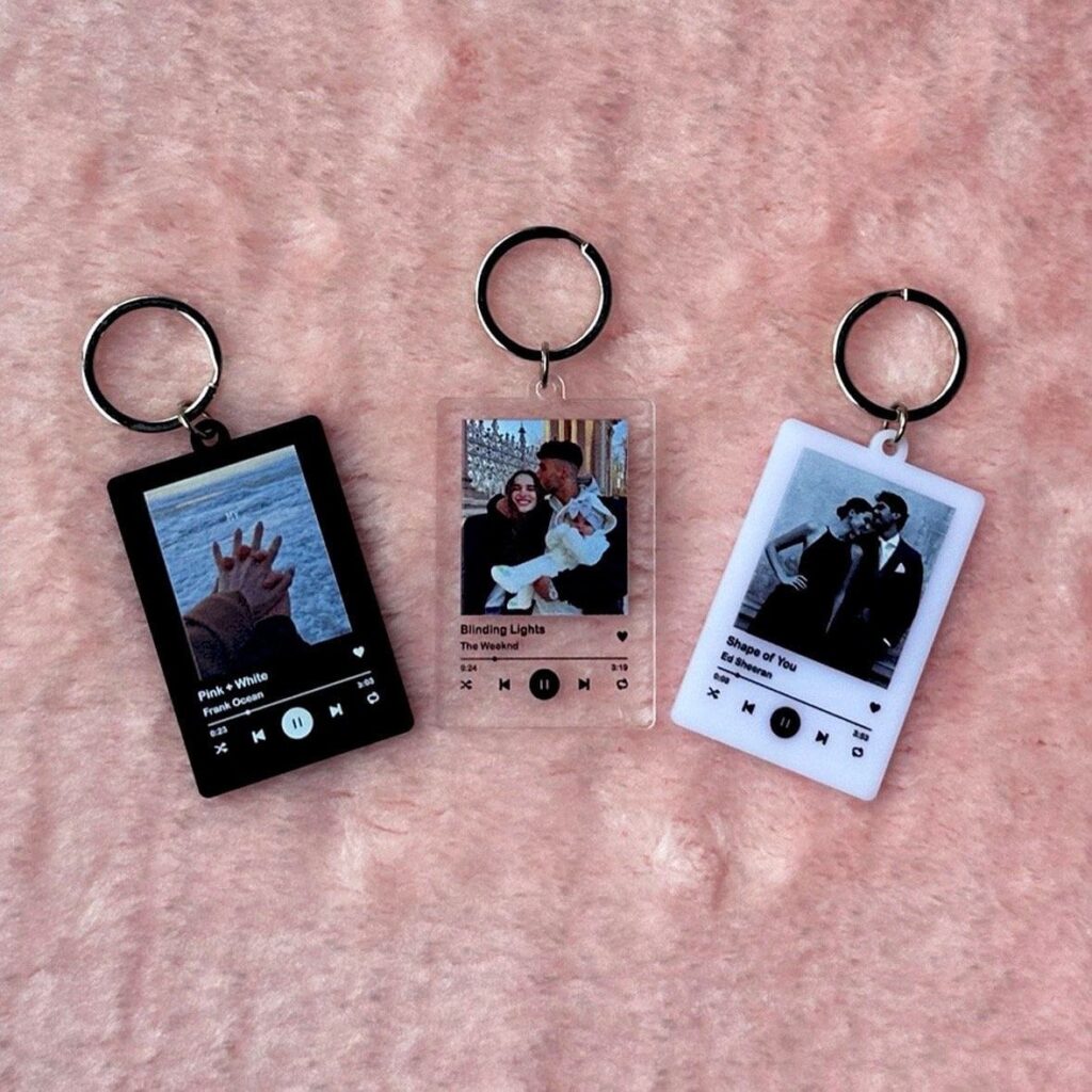 Custom music player keychains on pink background, featuring song titles and personal photos.