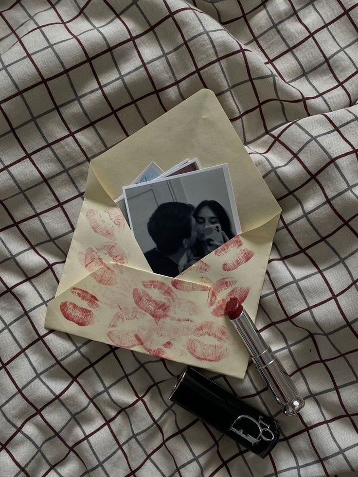 Envelope with lipstick marks, containing photos, a red lipstick on a checkered fabric background.