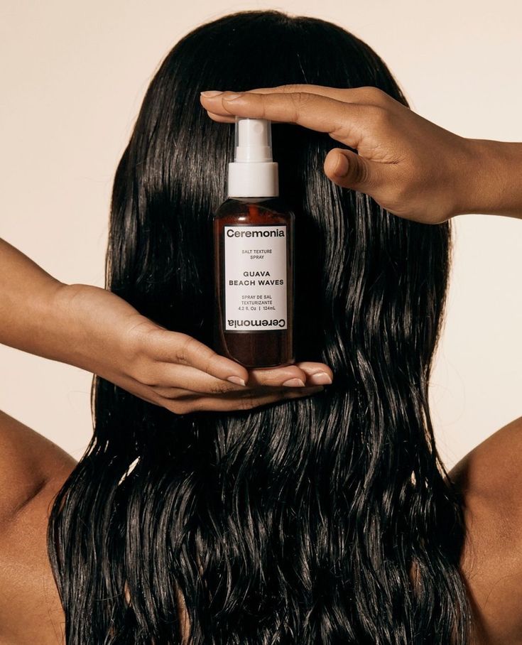 Person holding Ceremonia Guava Beach Waves spray against long, wavy hair.