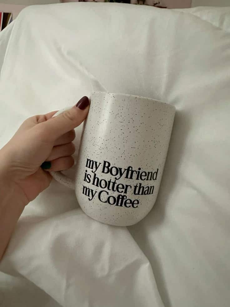 Hand holding a white mug with text: my Boyfriend is hotter than my Coffee against a white background.