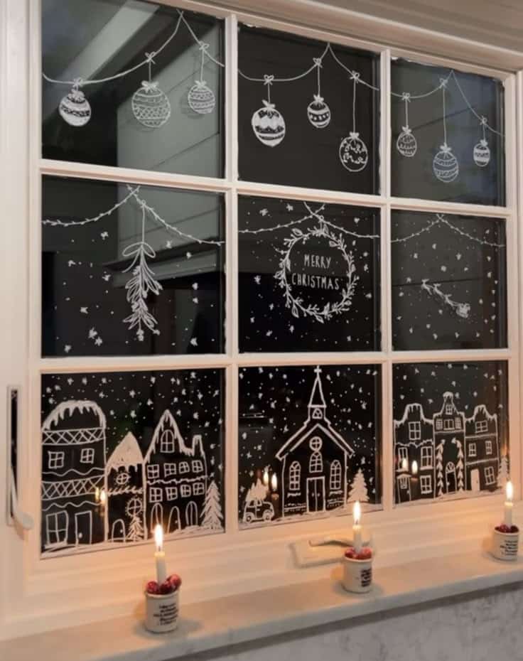 Festive window with hand-drawn Christmas village, ornaments, and candles, creating a cozy holiday atmosphere.