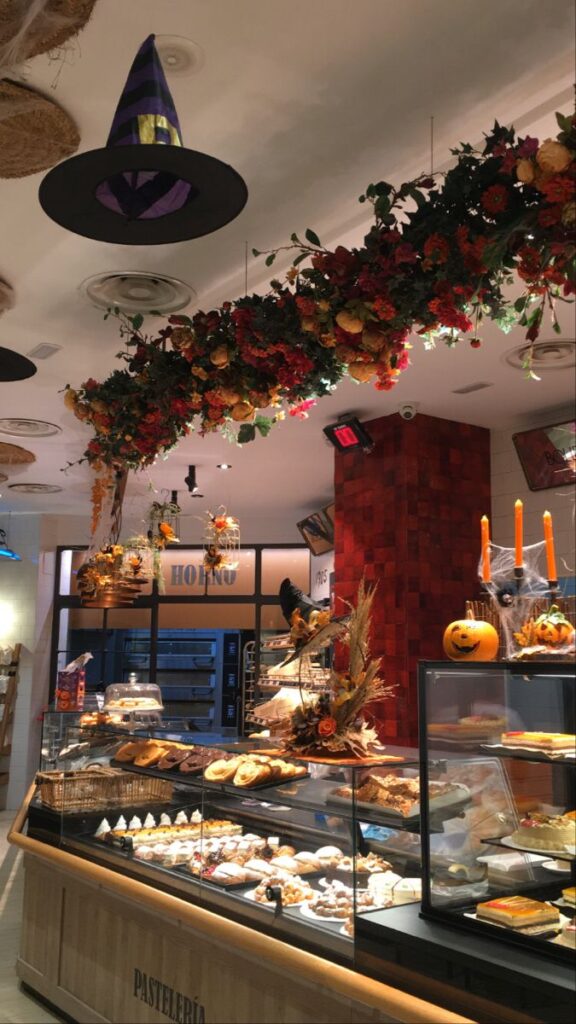 A Halloween inspired bakery Festive bakery display with Halloween decorations, floral garlands, and assorted pastries in a cozy setting. | Sky Rye Design Festive bakery display with Halloween decorations, floral garlands, and assorted pastries in a cozy setting.
