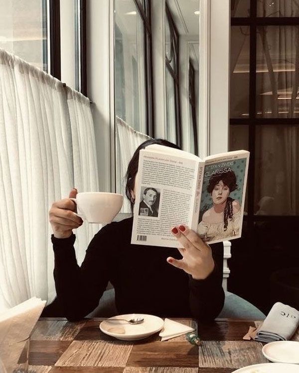 Person in cafe reading a book and holding a coffee cup, enjoying a peaceful moment by the window.