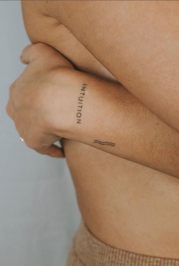 Minimalist forearm tattoos with the word 'Intuition' and wave design on person's arm.