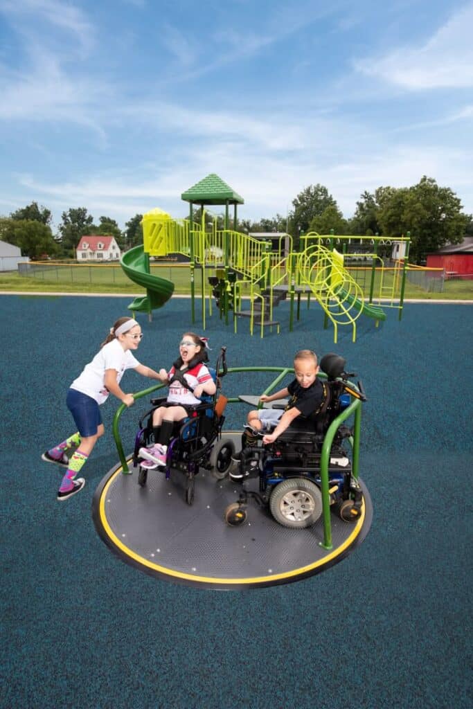 Children enjoying an accessible playground with inclusive equipment and a wheelchair-accessible merry-go-round.