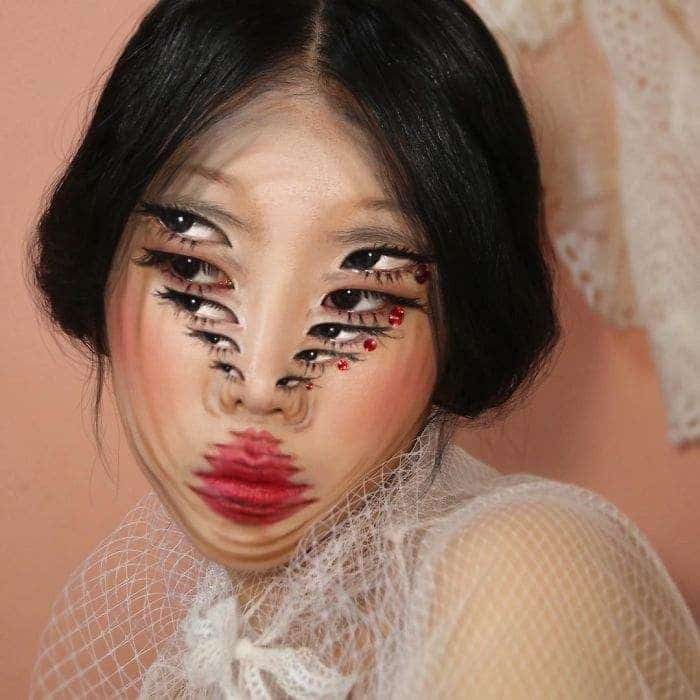 Surreal face makeup art with multiple eyes and lips, creating an optical illusion effect on a woman's face.
