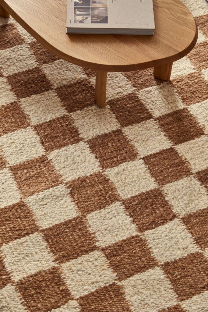 Checkered brown and beige rug beneath a wooden coffee table with a book, creating a cozy and stylish living room setting.