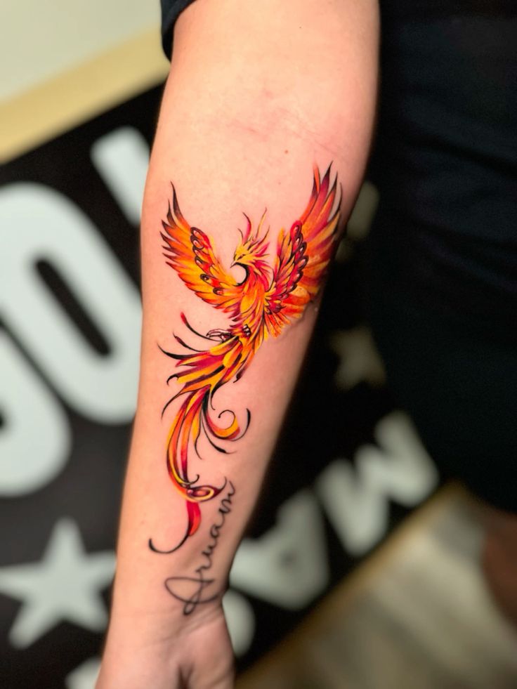 Vibrant phoenix tattoo in orange and red on a forearm with the word Dream written below it.