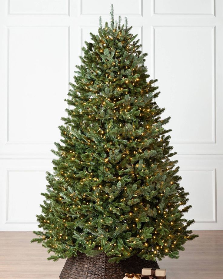 Decorated Christmas tree with warm white lights in a room with white paneled walls and wooden floor.
