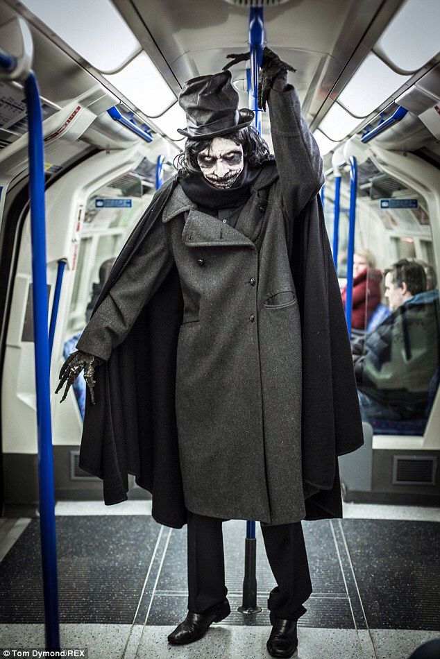 Person in a dark, Victorian-style costume on a subway, with white makeup and top hat, creating a mysterious vibe.