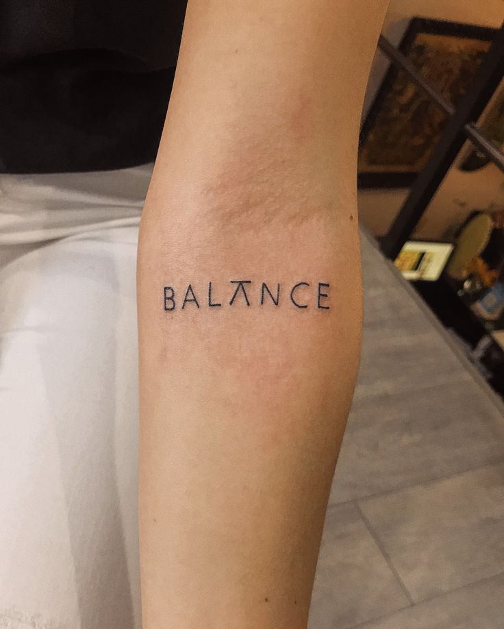 Tattoo of the word BALANCE on an arm, minimalistic design with unique A, symbolizing harmony and stability.