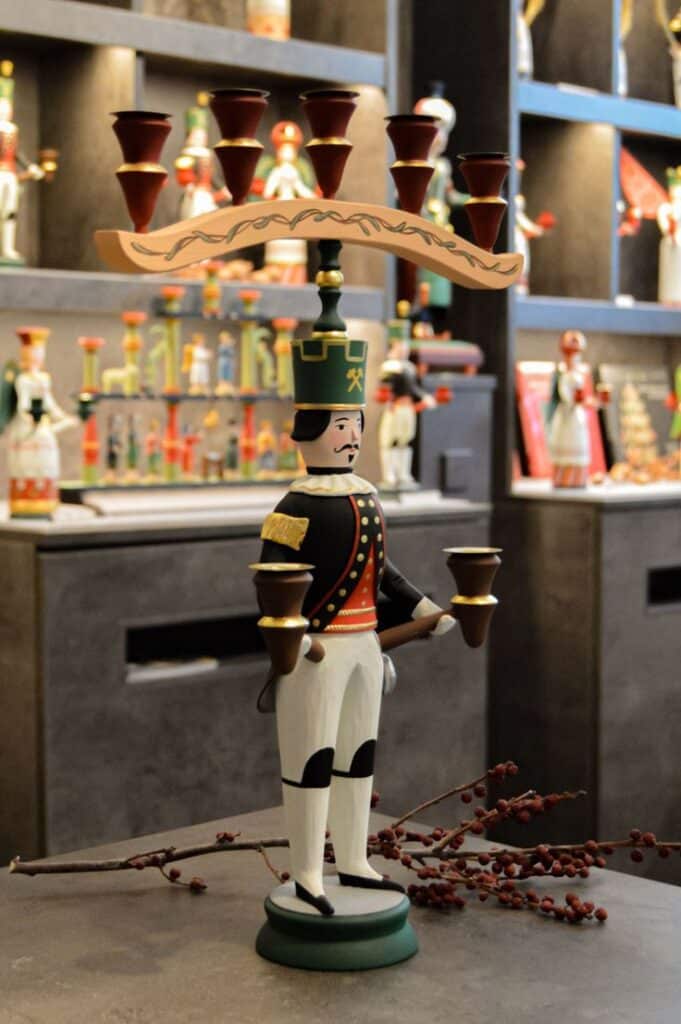 Bergmänner Wooden nutcracker soldier candle holder with decorative design, displayed on a shelf with other festive items. | Sky Rye Design Wooden nutcracker soldier candle holder with decorative design, displayed on a shelf with other festive items.