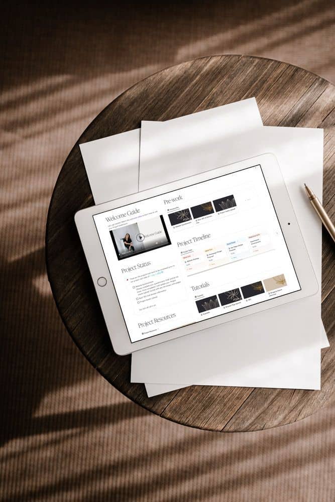 Tablet displaying project management software on a wooden table with papers and pen nearby.