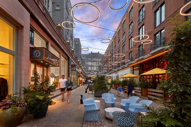 Outdoor urban shopping alley with modern ring lights and cafes, featuring people walking and vibrant store displays.