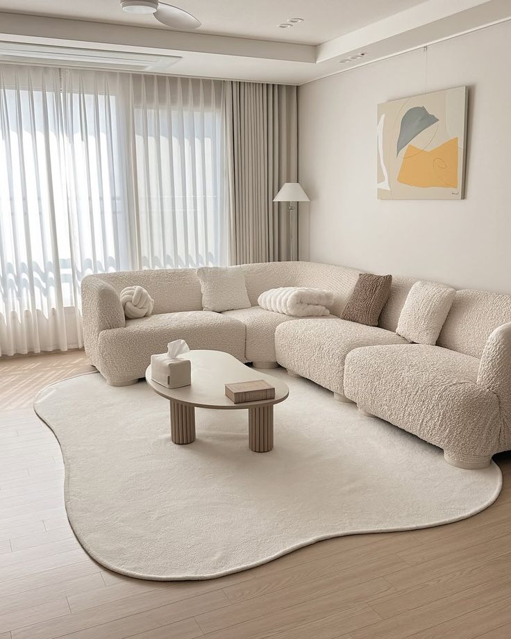 Minimalist living room with a cozy beige sectional sofa, modern art, and soft natural light from large windows.