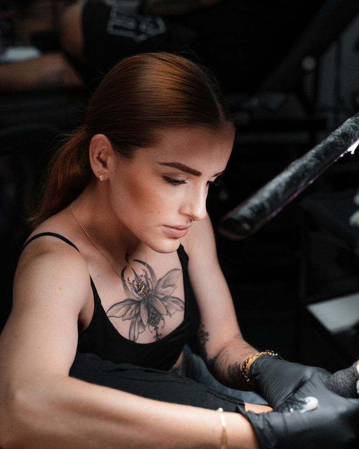 Tattoo artist focused on creating intricate floral design on client, wearing gloves and black top.