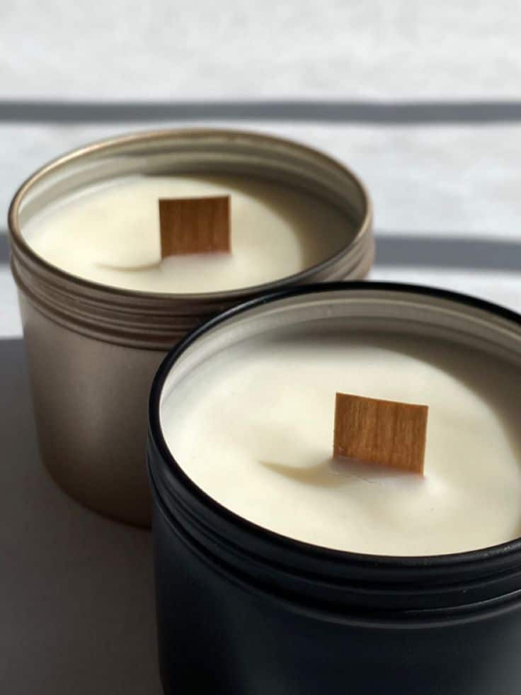 Two soy candles with wooden wicks in elegant metal containers on a light background.