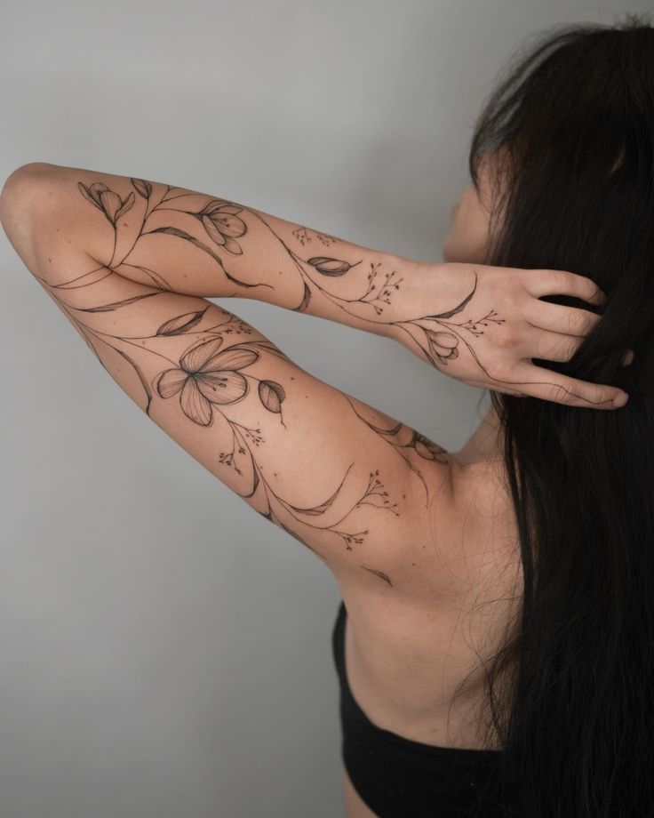 Woman with detailed floral arm tattoo, long hair, and black top, viewed from the side.
