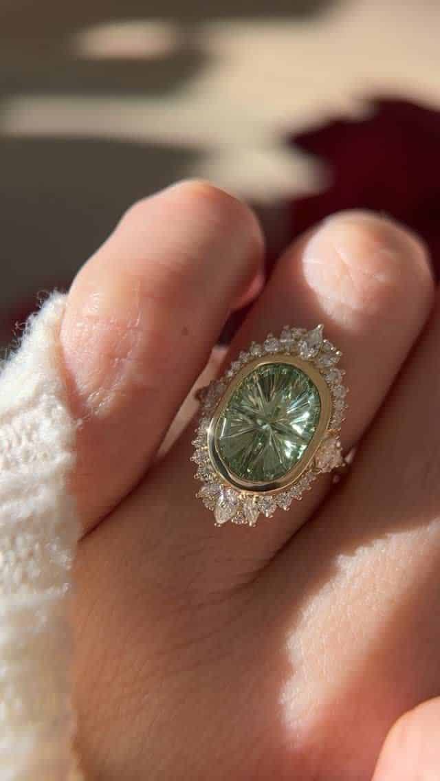 Brianna Trudell _ How is this my real life job_ 😭 Elegant green gemstone ring with diamond halo on finger, capturing sparkle in natural light. | Sky Rye Design Elegant green gemstone ring with diamond halo on finger, capturing sparkle in natural light.