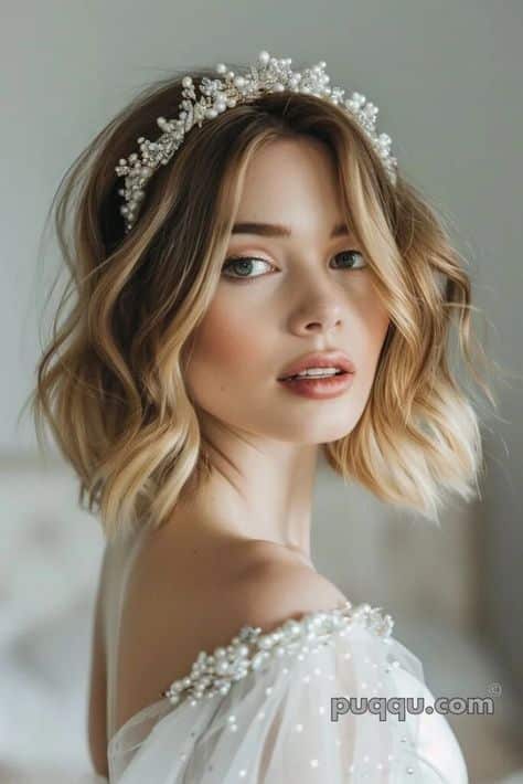 Young woman with short blonde hair wearing a pearl headband and an off-shoulder dress, looking over her shoulder.