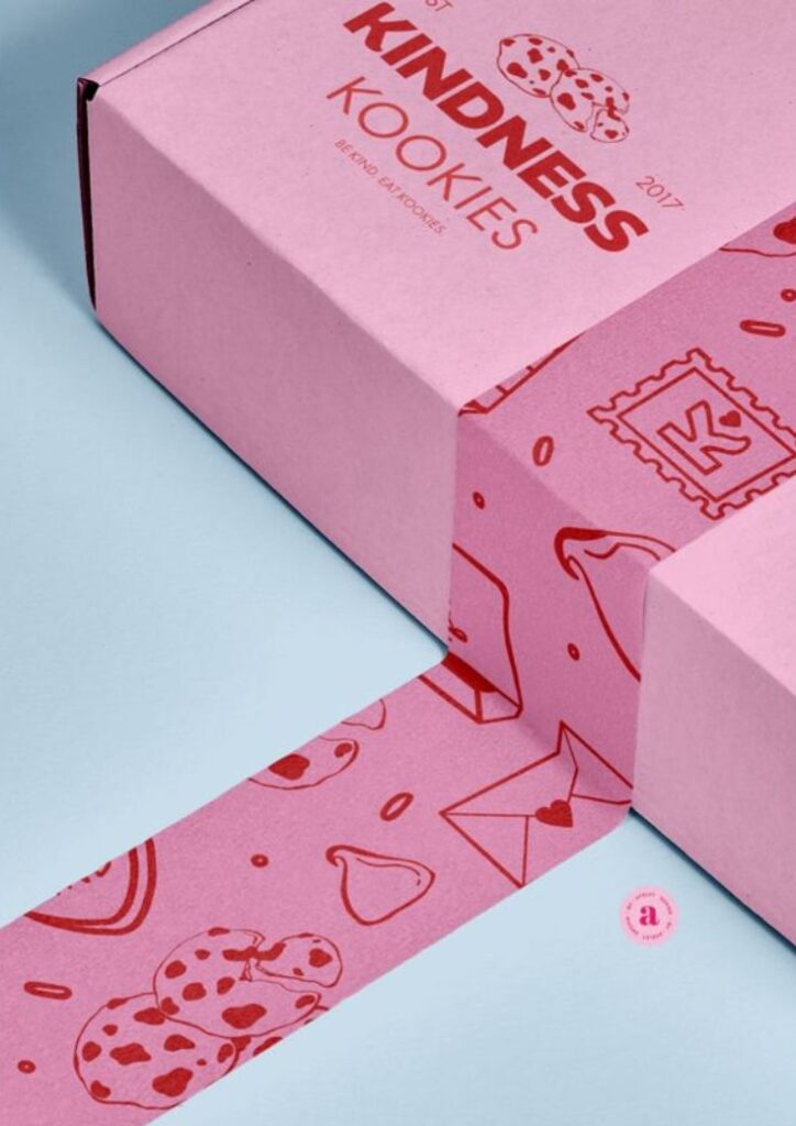 Pink Kindness Kookies box on blue background with decorative tape featuring cookies and envelopes.