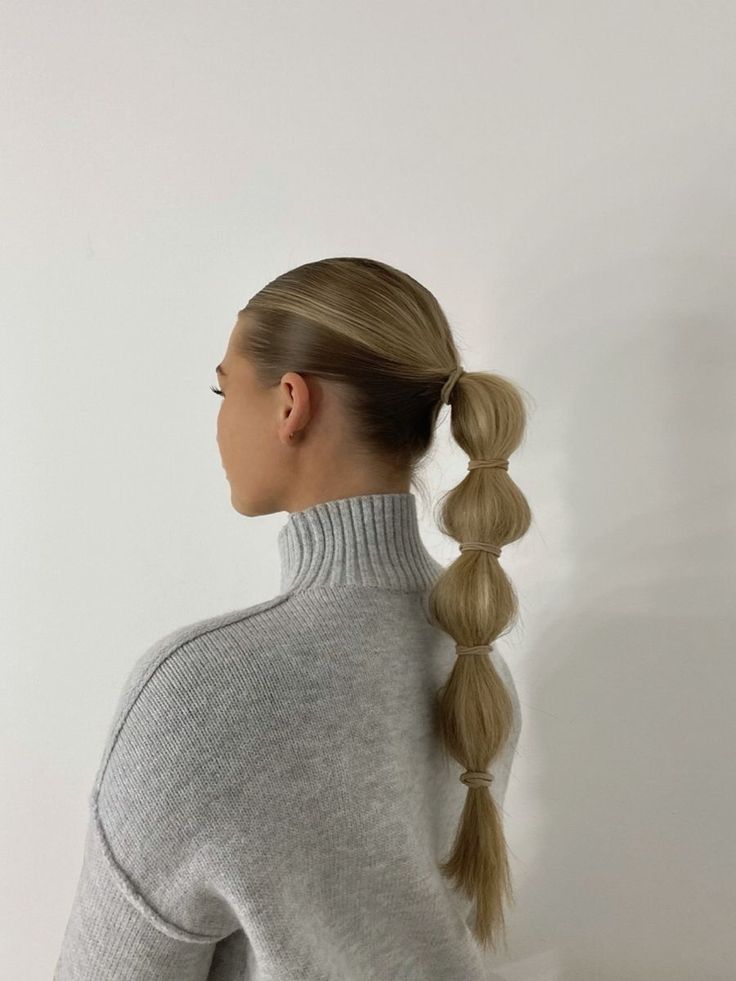 Woman with sleek bubble ponytail hairstyle in gray turtleneck sweater, facing sideways.