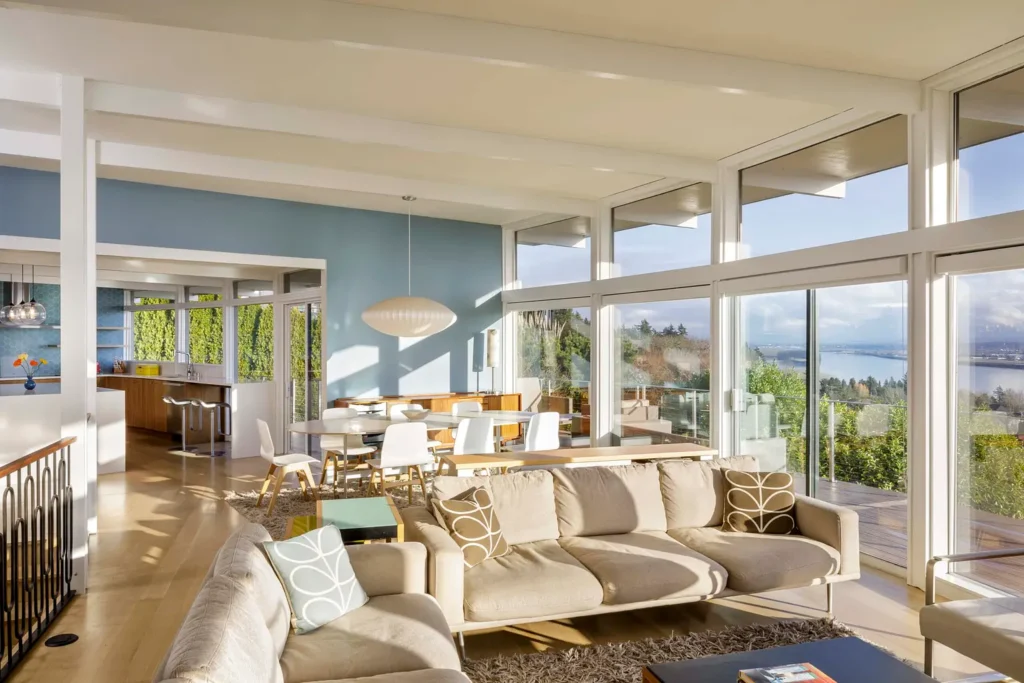 Buena-Vista-Curved-Home-Remodel-Hammer-Hand-scaled Modern living room with large windows, ocean view, beige sofa, and dining area with natural light. | Sky Rye Design Modern living room with large windows, ocean view, beige sofa, and dining area with natural light.