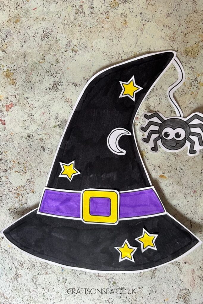 Cartoon witch hat with purple band, yellow stars, moon, and a cute spider hanging on a textured background.