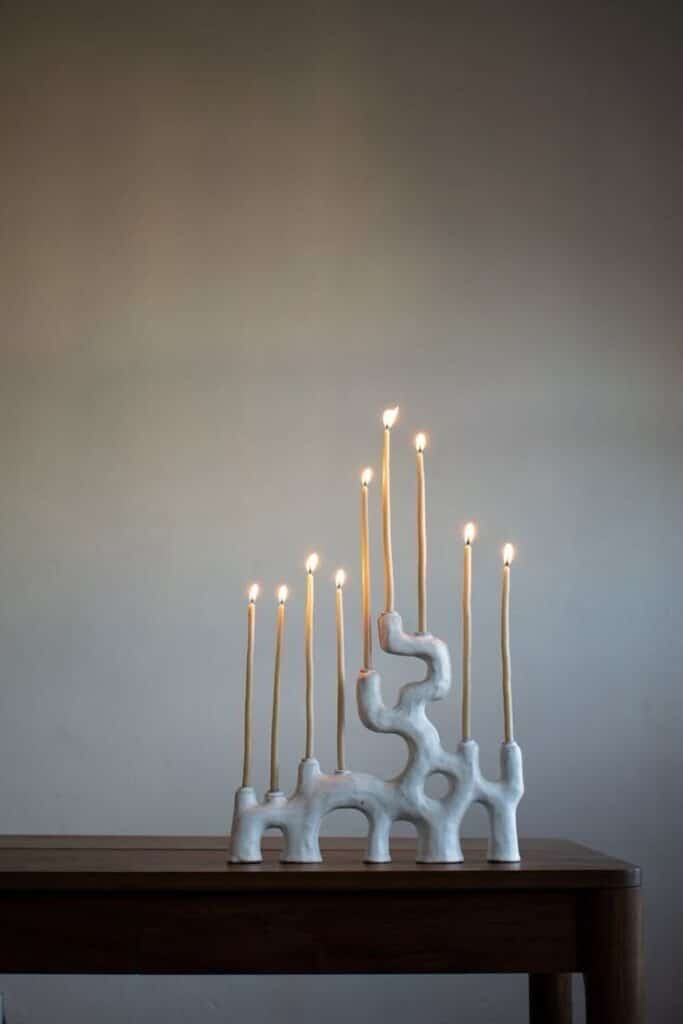 Sculptural white ceramic candle holder on wooden table with lit candles creates warm, atmospheric glow.