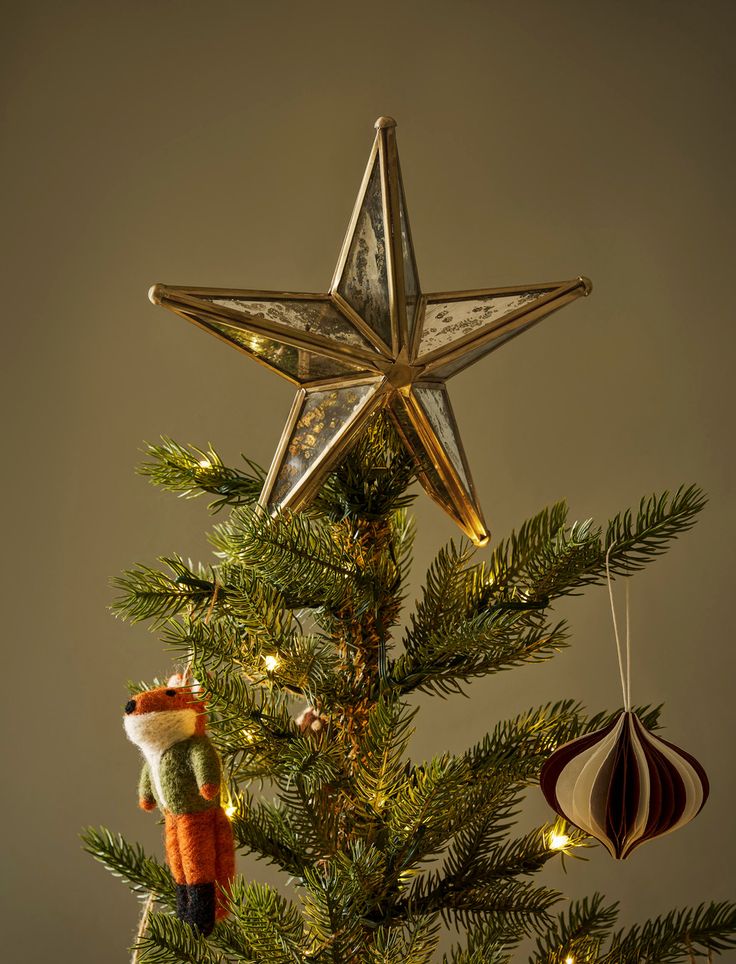 Christmas tree top with star topper, hanging fox ornament, and decorative bauble, surrounded by twinkling lights.