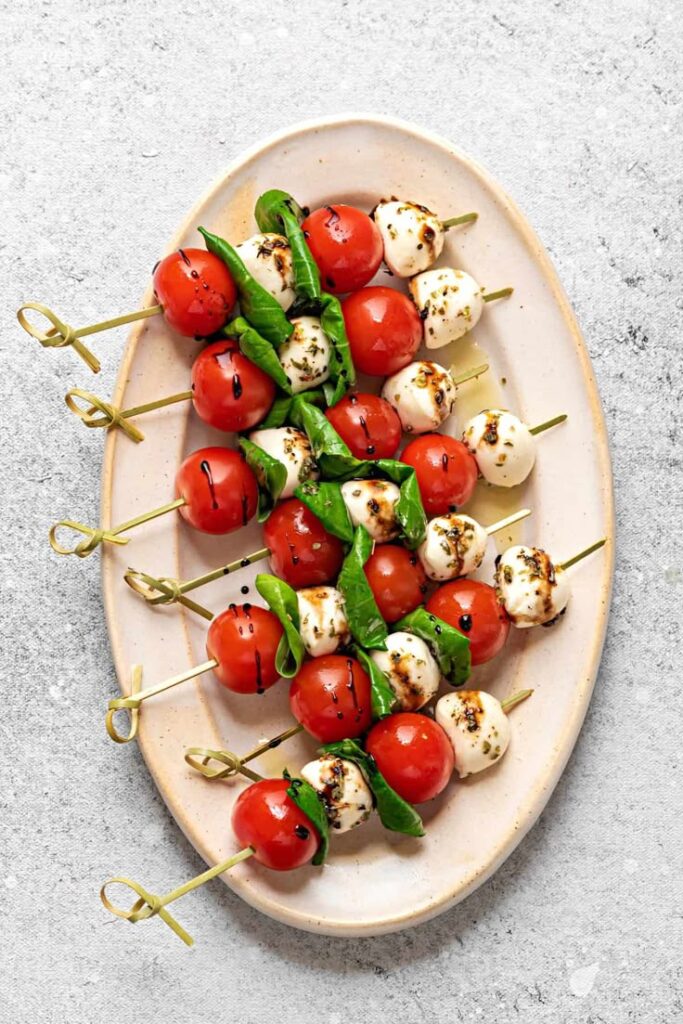 Caprese skewers with cherry tomatoes, mozzarella, basil, and balsamic glaze on a plate.