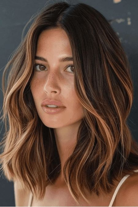 Woman with shoulder-length brown hair with highlights on a dark background.