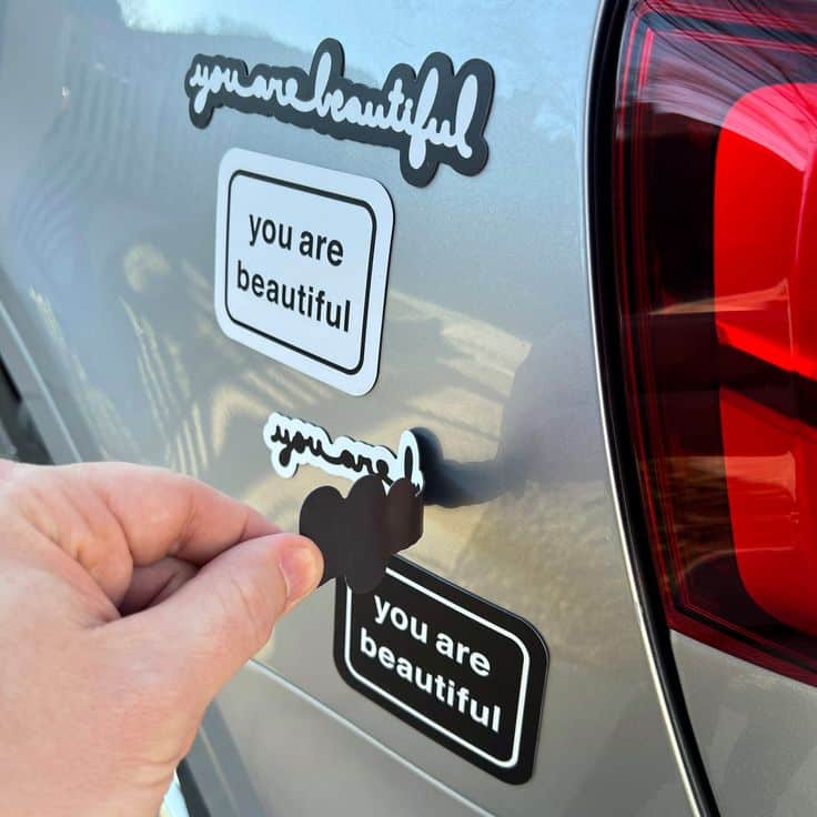 Hand placing you are beautiful stickers on a gray car, promoting positivity and self-love.