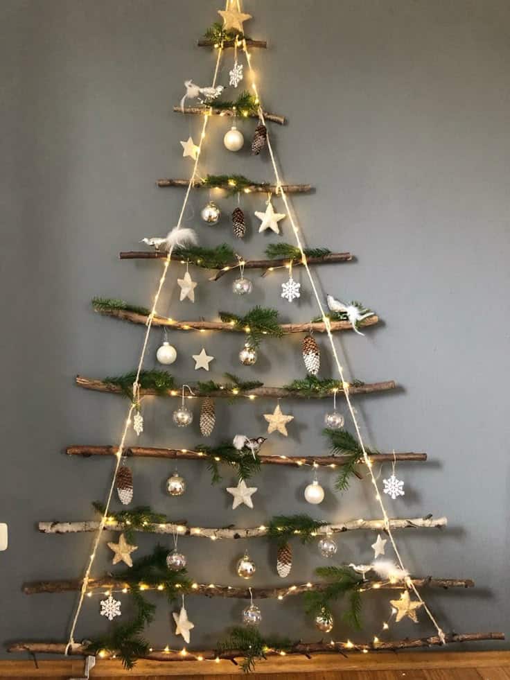 Rustic wall-mounted Christmas tree with branches, ornaments, and lights on gray background. Cozy and festive decor.