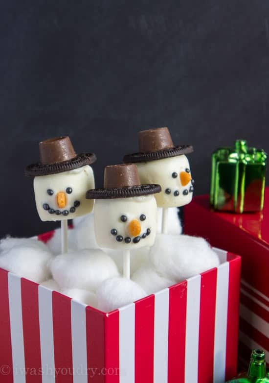 Festive marshmallow snowmen pops with hats in a striped box, perfect for holiday treats and Christmas decoration ideas.