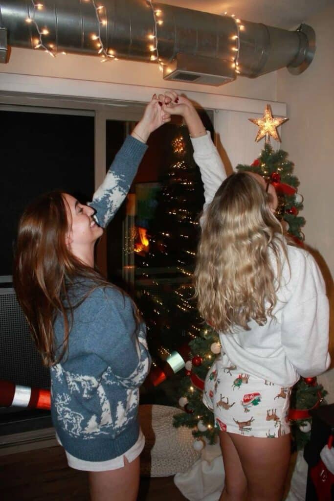 Two friends celebrate Christmas, decorating a tree with lights and joy in a cozy room.
