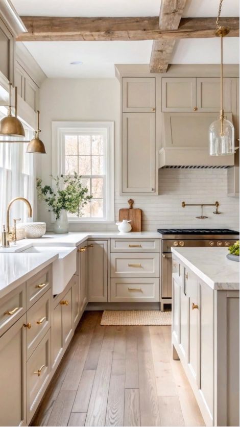 Stylish modern kitchen with beige cabinets, rustic wood beams, and gold accents bathed in natural light.