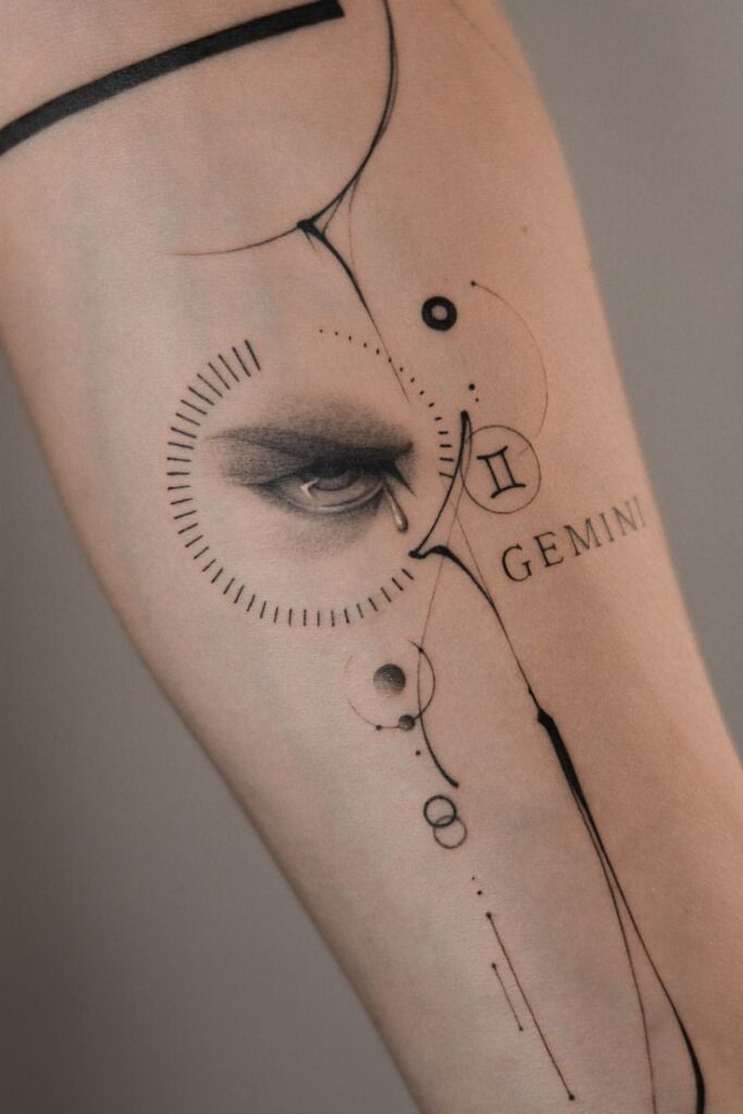 Abstract Gemini tattoo featuring an eye and geometric designs on forearm. Elegant and artistic zodiac body art.