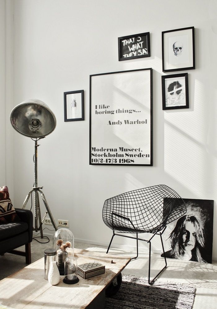 Modern living room with eclectic wall art, sofa, industrial lamp, wire chair, and coffee table decor.