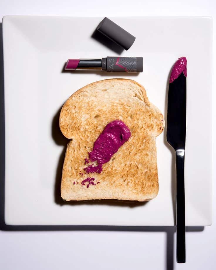 Lipstick smeared on toast with a knife on a white plate, blending beauty and food concepts.