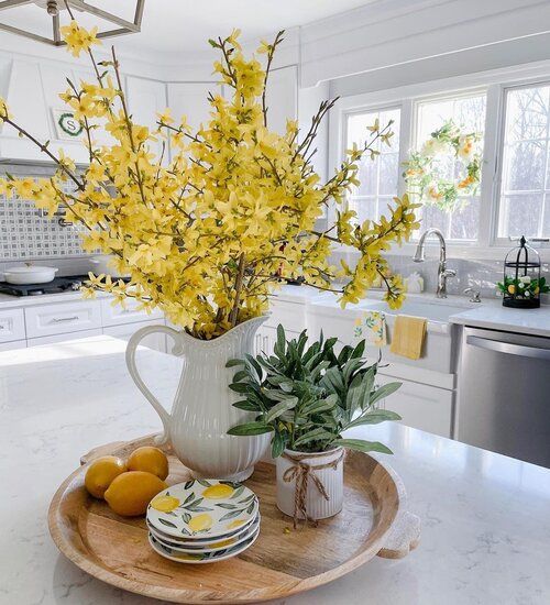 Yellow forsythia and herbs in a white kitchen, with lemons and plates on a tray, create a bright, fresh spring vibe.