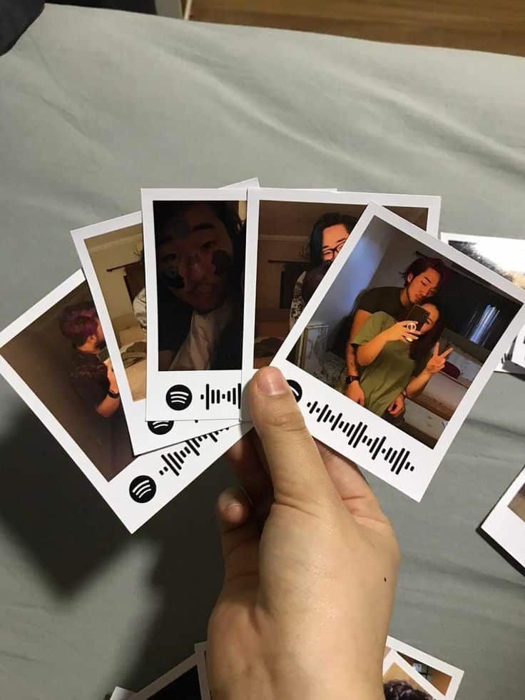 Hand holding Polaroid photos with Spotify codes, featuring friends posing and an indoor setting.