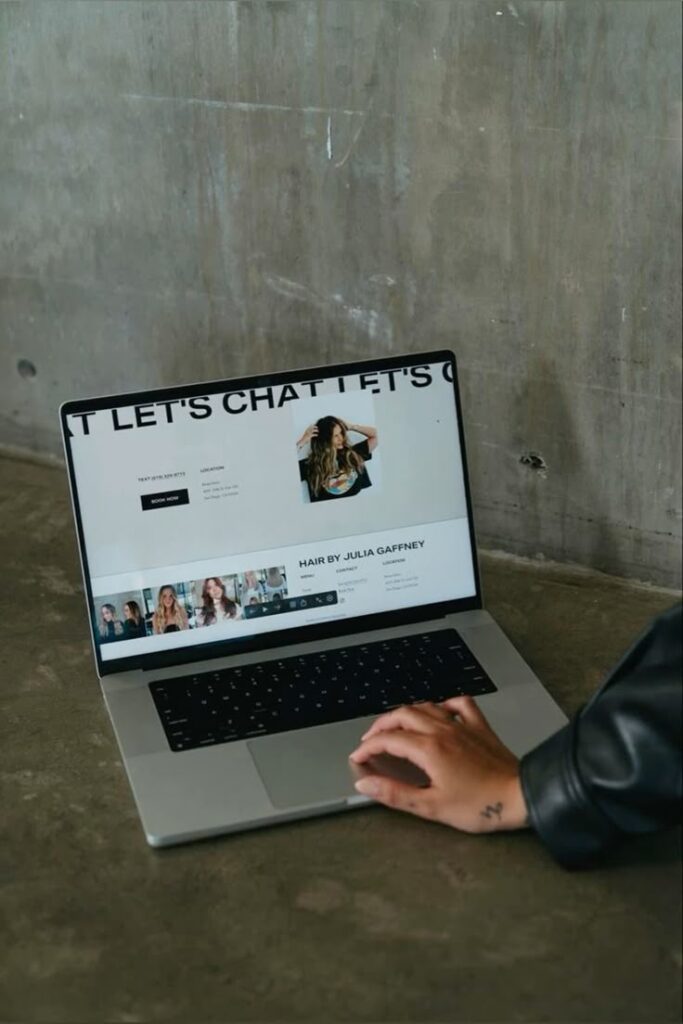 Person browsing hairstylist portfolio on laptop, featuring salon services and booking info.