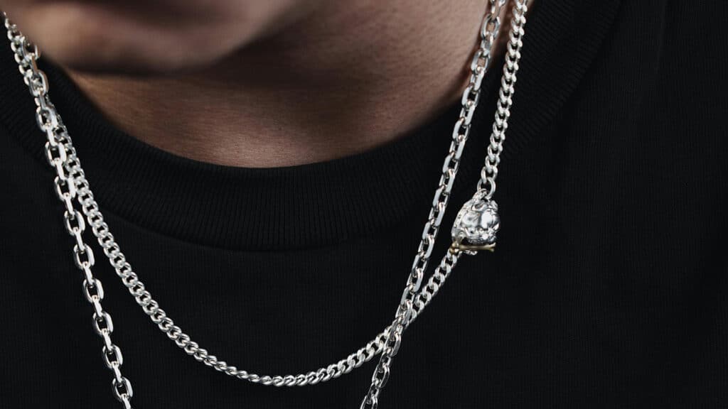 Close-up of layered silver chains with a skull pendant against a black shirt.