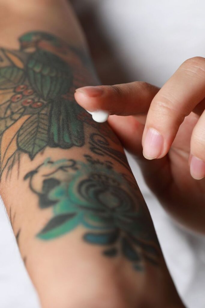 Applying cream to colorful arm tattoo for aftercare and skin hydration.