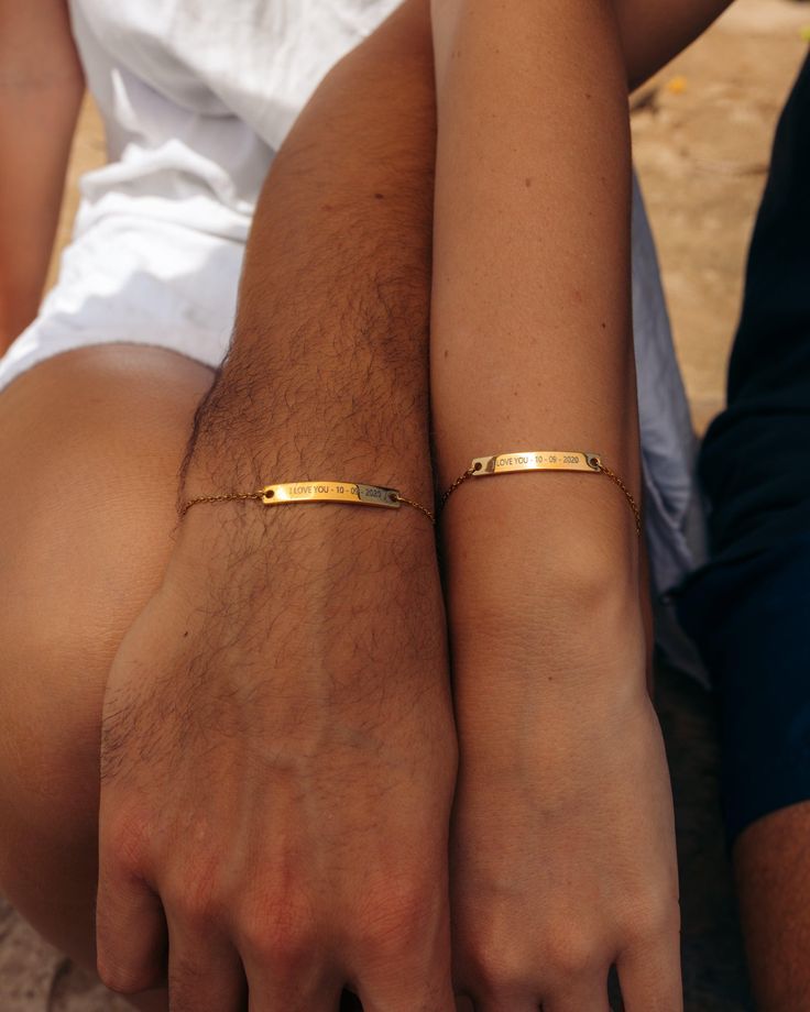 Couple wearing matching gold engraved bracelets with I love you message and date, showing their arms side by side.