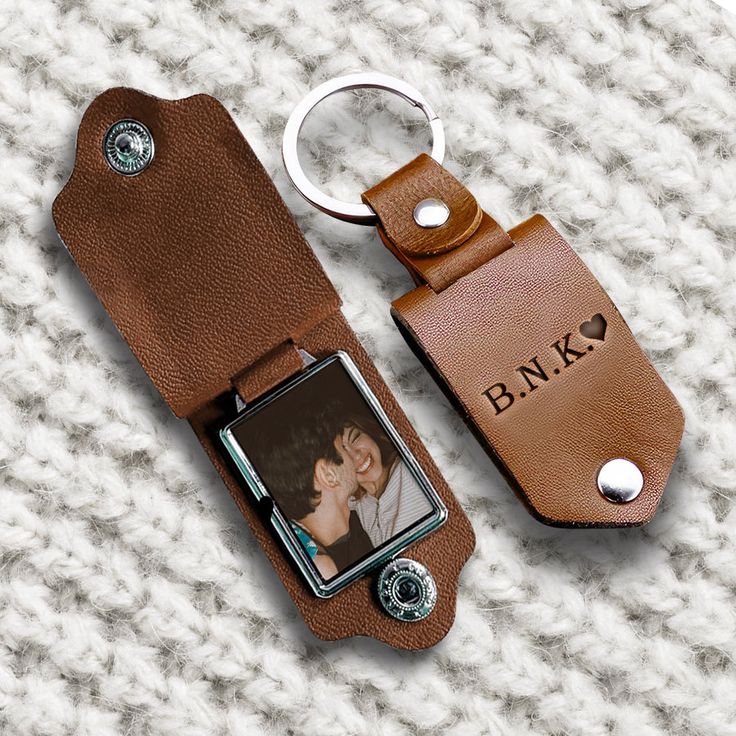 Brown leather keychain with photo compartment on textured fabric background, engraved with B.N.K. and heart symbol.