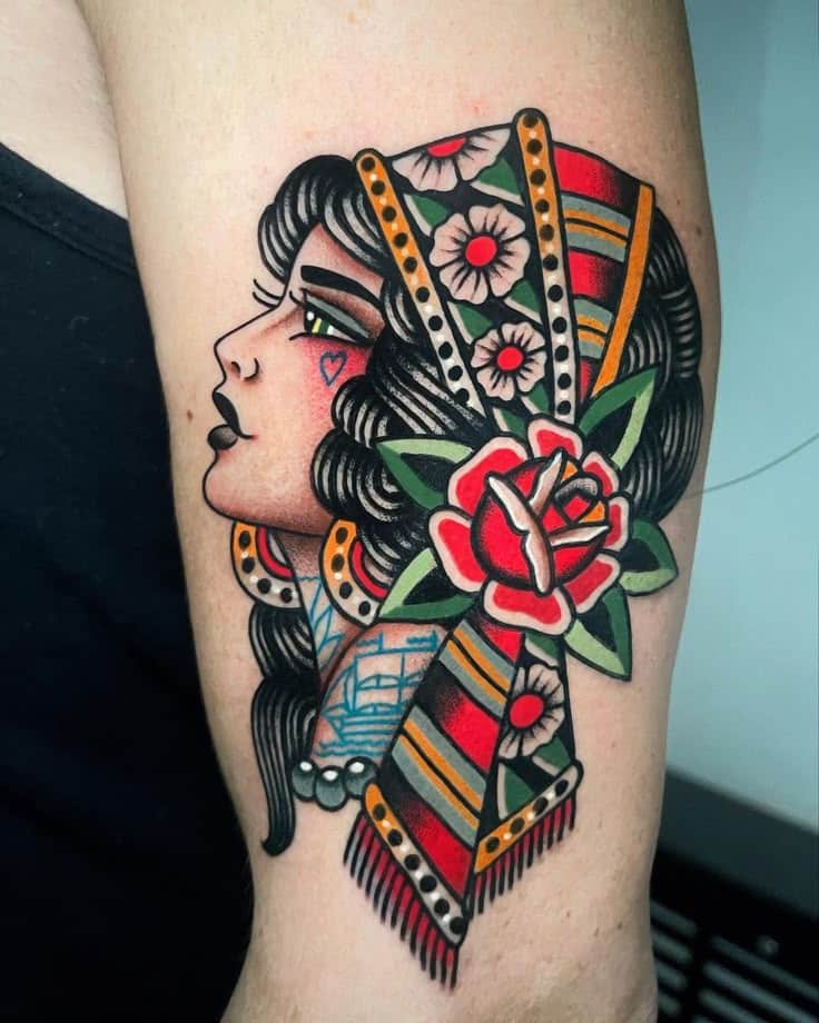 Colorful traditional tattoo of a woman in profile with floral decoration and vibrant patterns on upper arm.